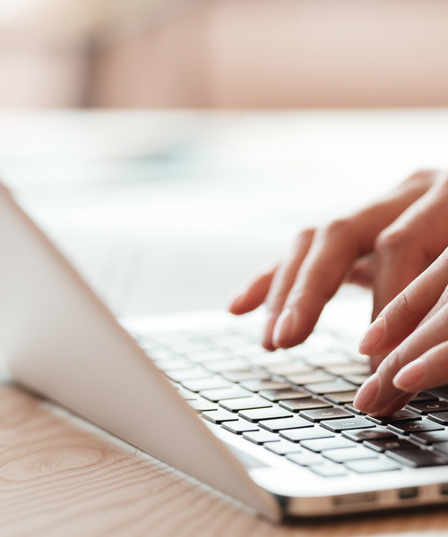 Nahaufnahme von Händen, die auf einer Laptop-Tastatur tippen.