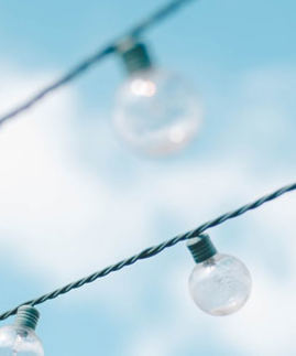 Lichterkette mit runden Glühbirnen vor blauem Himmel mit weißen Wolken.