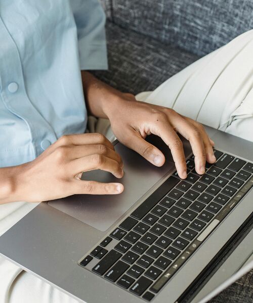 Nahaufnahme von Händen, die auf einem Laptop auf dem Schoß tippen.