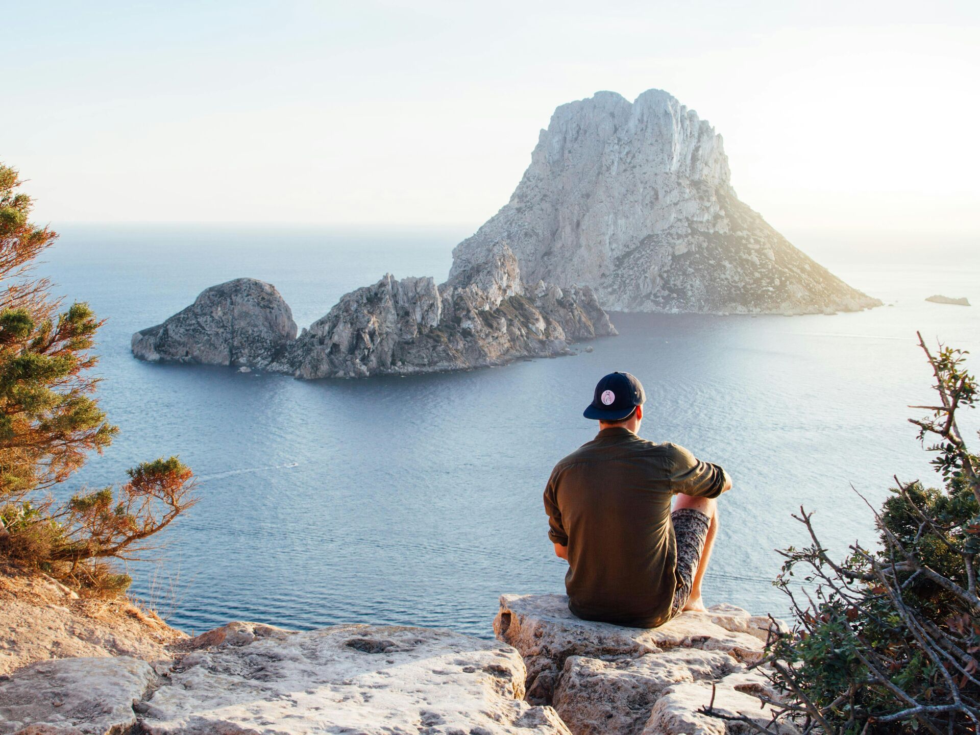 Person sitzt auf einem Felsen und blickt auf das Meer und eine vorgelagerte Insel.