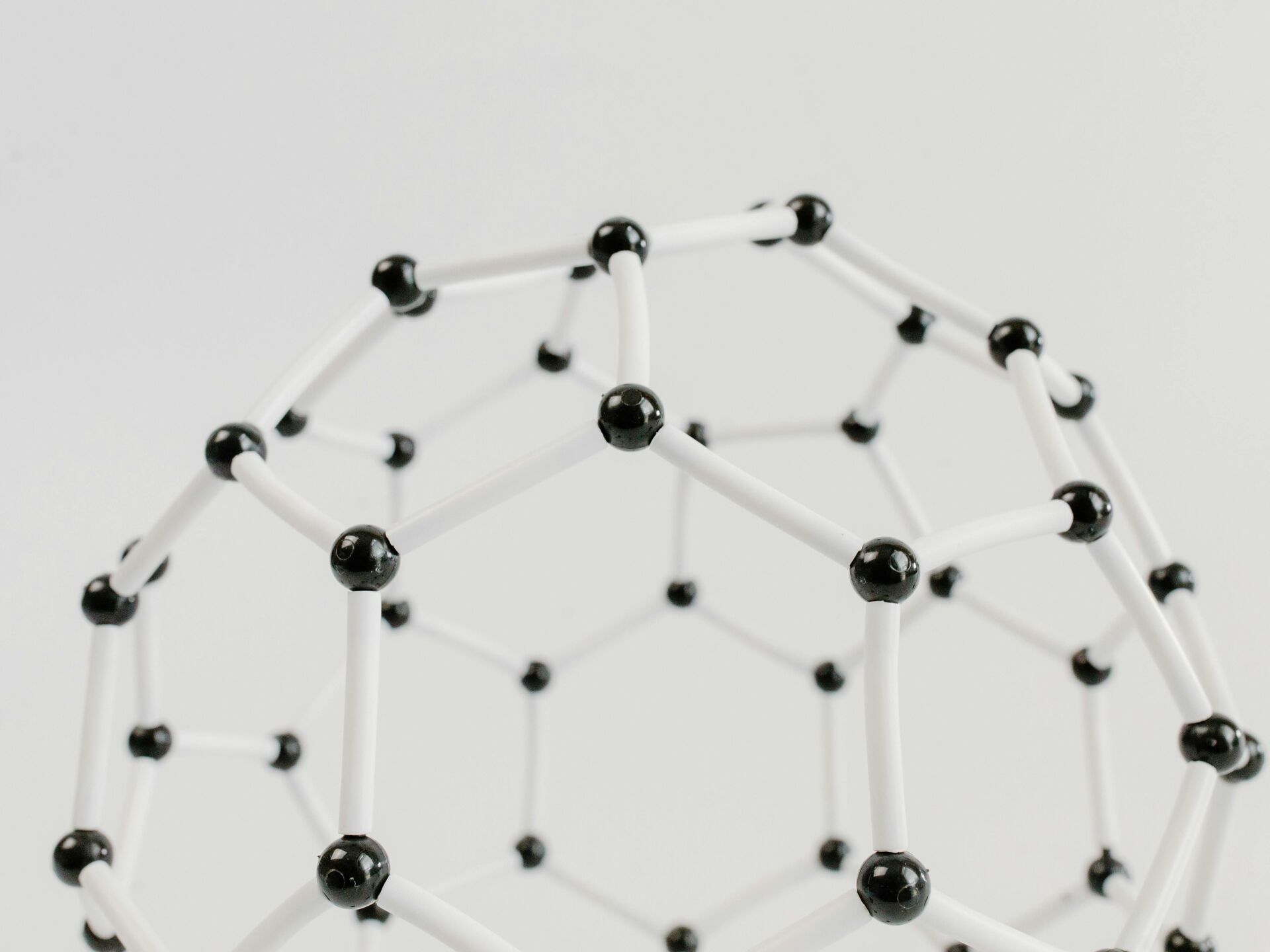 Abstraktes Modell einer Molekülstruktur aus weißen Stäben und schwarzen Verbindungspunkten auf hellem Hintergrund.