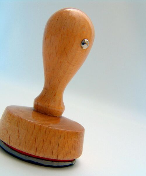 Holzstempel mit rundem Griff auf hellem Hintergrund, leicht schräg positioniert.