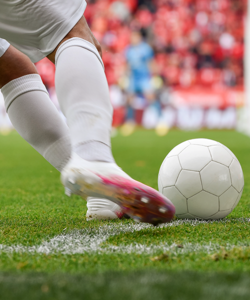 Fußballspieler in weißem Trikot schießt den Ball von der Seitenlinie auf dem Spielfeld.