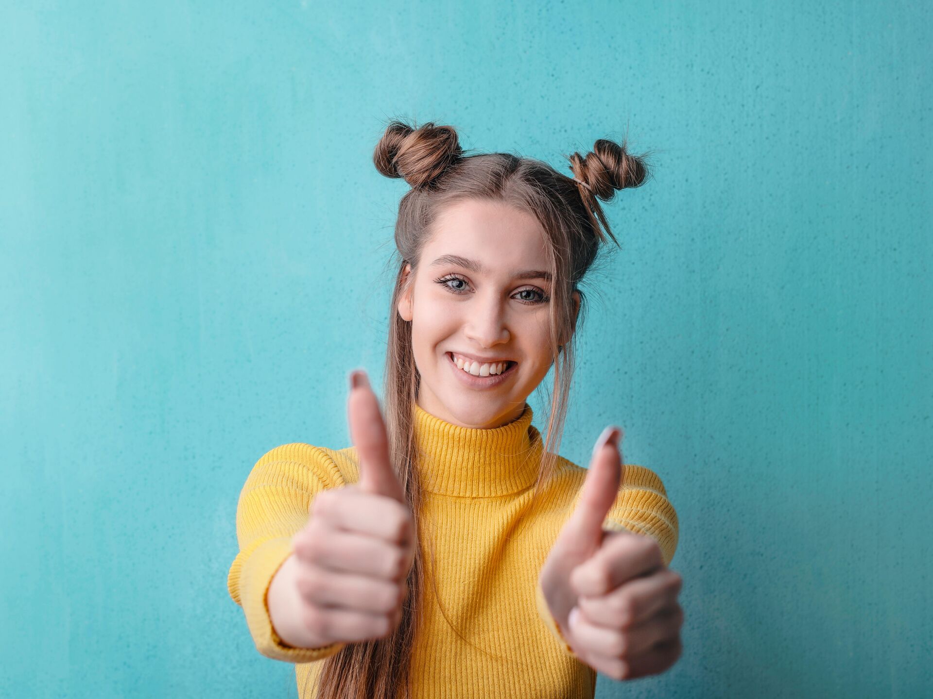 Lächelnde Person zeigt beide Daumen nach oben vor einer türkisfarbenen Wand.
