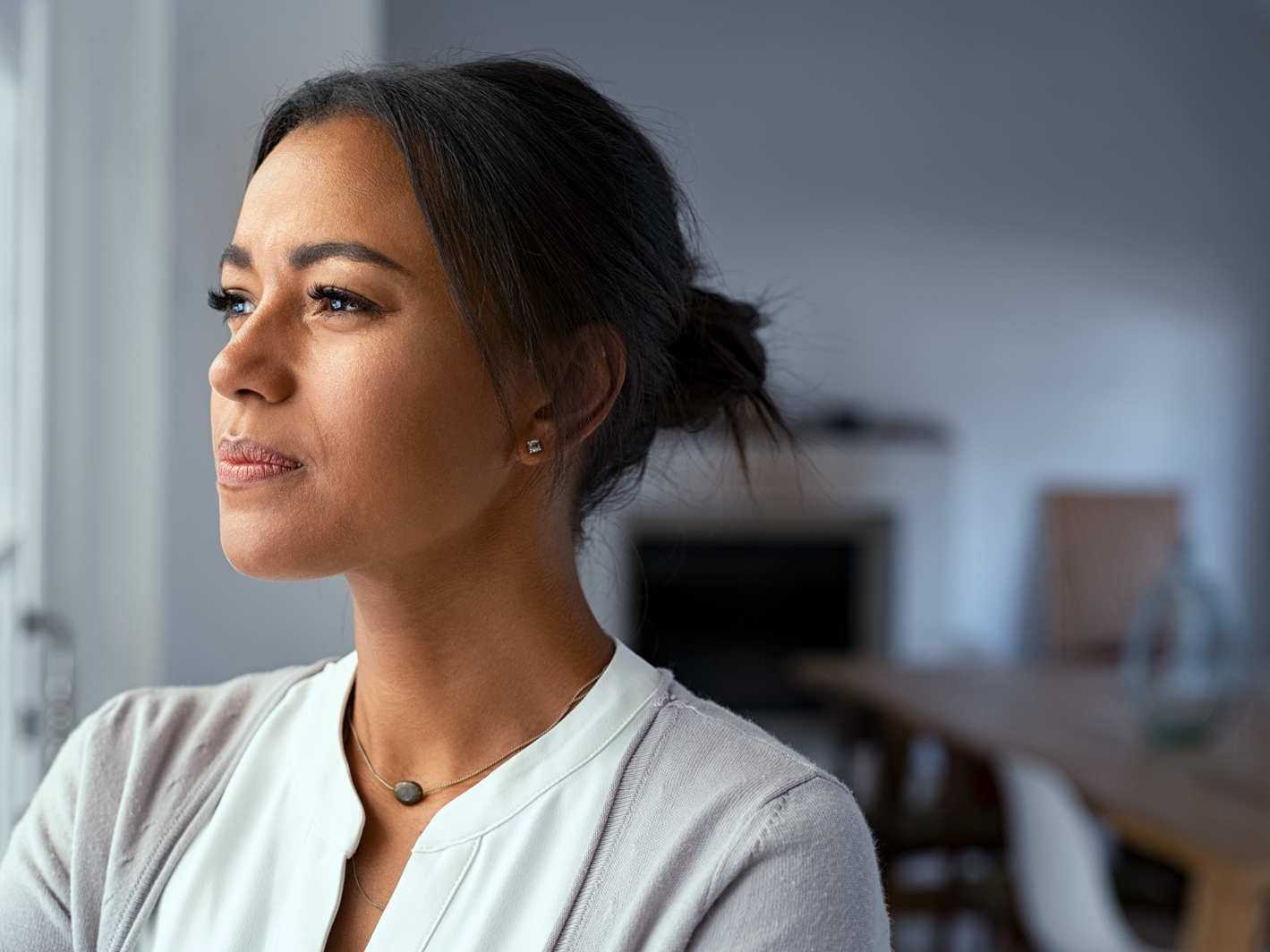 Porträt einer nachdenklich blickenden Frau in heller Kleidung in einem Innenraum.