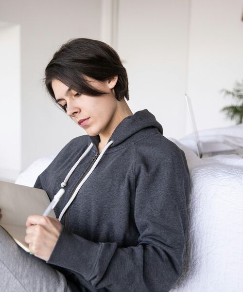 Person sitzt entspannt auf dem Sofa und schreibt konzentriert in ein Notizbuch.