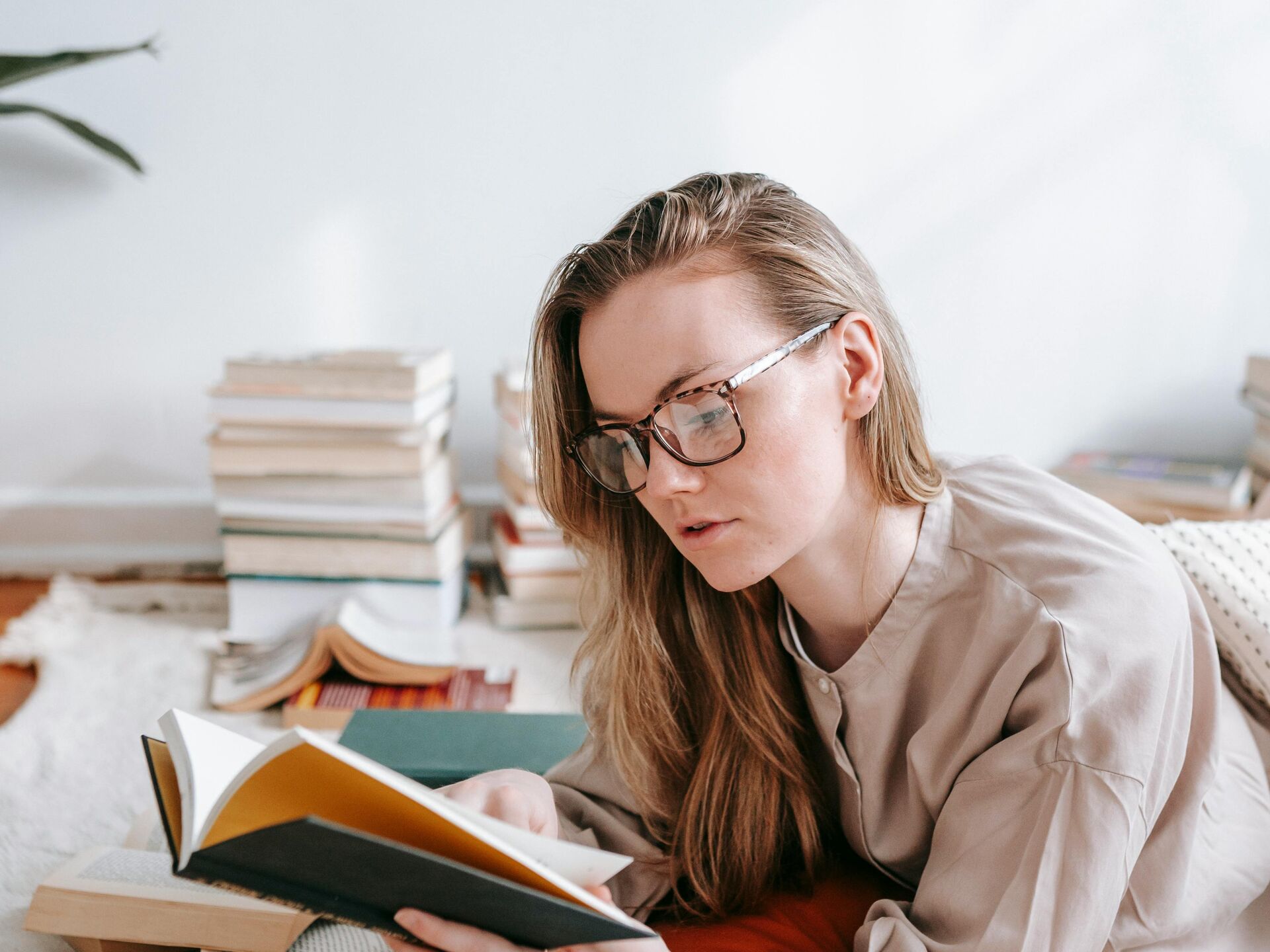 Person liegt entspannt auf dem Boden, liest ein Buch und ist umgeben von mehreren aufgeschlagenen Büchern.