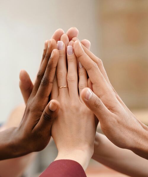 Mehrere Hände berühren sich in der Mitte als Zeichen für Zusammenhalt und Teamgeist.